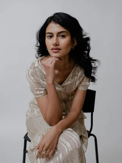 A full portrait of the model sitting, showing the complete look. The subtle makeup and soft hairstyle create a timeless and sophisticated image.