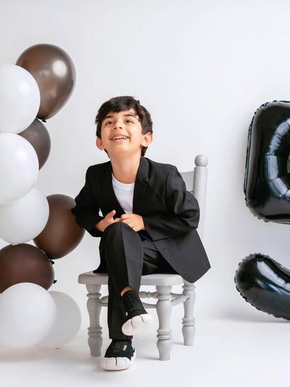 Celebrating a fifth birthday in style! This young boy looks so dapper and happy in his milestone photoshoot, complete with balloons and a smart suit.
