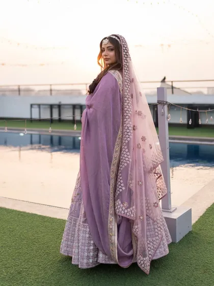 The bride looking over her shoulder, her veil and lehenga creating a beautiful silhouette against the evening sky.