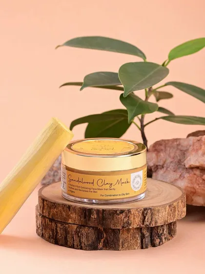 A shot of Pure by Priyanka's Sandalwood Clay Mask, styled with a piece of sandalwood and natural props. This visual setup communicates the key ingredient and the product's earthy origins.