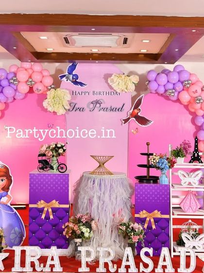 A Sofia the First party setup featuring a pink and purple balloon arch and cutouts of the princess and her animal friends.