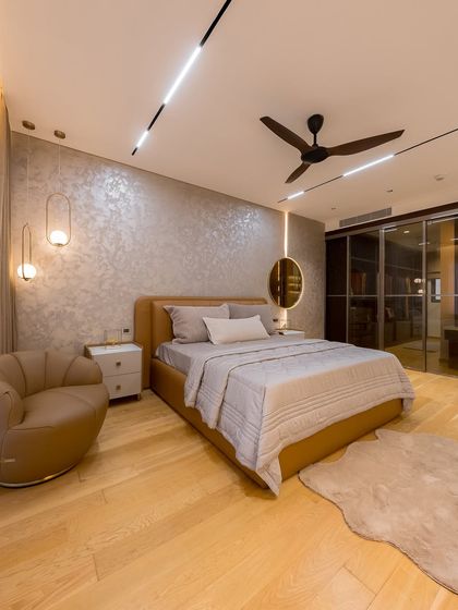 This exquisite master bedroom is a perfect blend of sophistication and comfort. A textured accent wall with a soft metallic finish, a plush tan leather headboard, and warm ambient lighting create the ultimate sanctuary for relaxation.