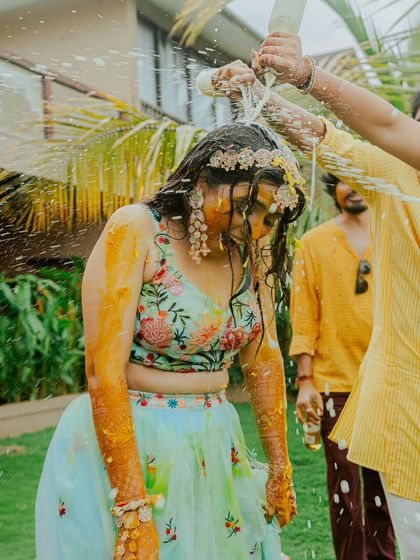The bride's turn for the buttermilk shower, a moment of surprise and laughter during the playful Haldi rituals.
