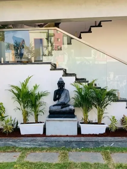 We create serene, tropical-themed corners that bring a sense of peace to your garden. This design features a black marble Buddha statue as a focal point, flanked by Areca palms in clean white planters and set against a backdrop of natural grass and stepping stones.