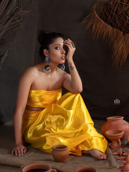 A portrait that captures a thoughtful moment from the earthy studio shoot. The bright yellow of the outfit stands out beautifully against the dark, moody background and rustic props.
