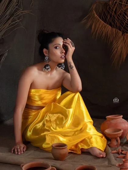 A portrait that captures a thoughtful moment from the earthy studio shoot. The bright yellow of the outfit stands out beautifully against the dark, moody background and rustic props.