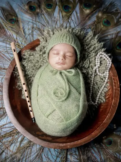 A serene Little Krishna themed portrait, one of our most requested cultural setups. This overhead shot showcases the beautiful arrangement of peacock feathers, a traditional flute, and the peacefully sleeping baby.