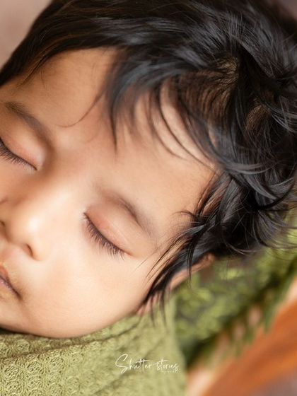 A close-up on this newborn's beautiful hair and peaceful sleeping face, wrapped in an olive green waffle wrap.