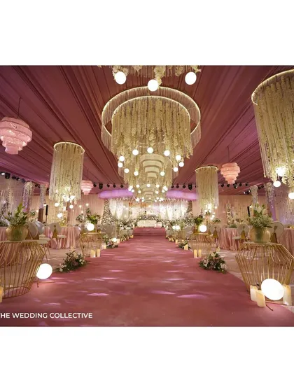 For this 'Midsummer Dream' reception, we created a magical, ethereal ambiance. The hall is dominated by grand, custom-made chandeliers dripping with thread curtains and flowers, casting a warm glow over the blush-pink decor and demonstrating our expertise in lighting and custom fabrication.