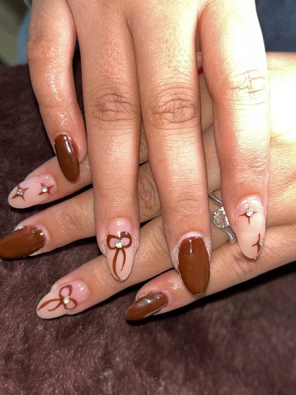 Some December nail inspo for you. This cute set features brown nails with hand-painted bow and star details.