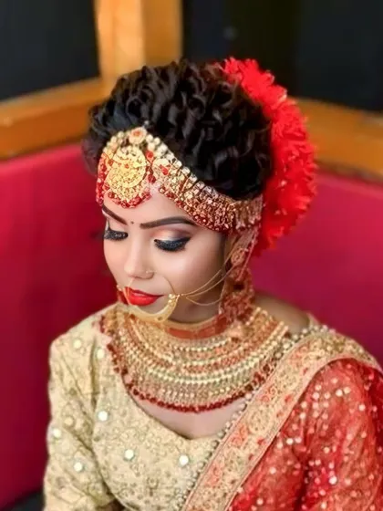 This is a classic bridal updo, perfect for a traditional wedding. The hair is styled in tight curls and adorned with a beautiful matha patti and red flowers to match the bride's attire.