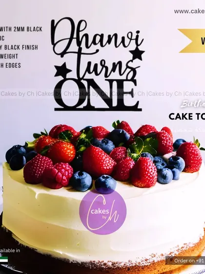 A mockup of the "Dhanvi Turns ONE" topper in black on a fruit-topped cake, demonstrating a classic and elegant combination.