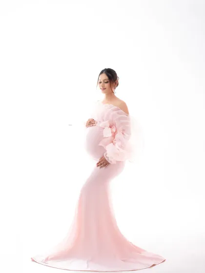 Pretty in pink. This high-key studio shot features a mother-to-be in a soft pink gown with delicate ruffled sleeves, creating a light and airy feel.