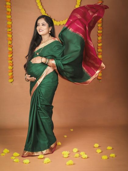 A beautiful mom-to-be in a green and pink silk saree, with her pallu flowing gracefully. The traditional marigold flower decorations add a festive and cultural touch to this maternity portrait.