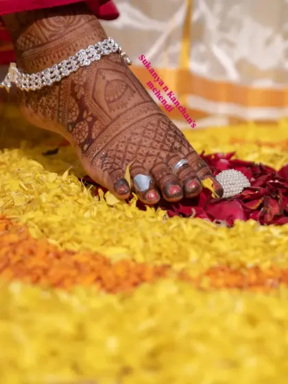 A close-up of a bride's foot, adorned with mehendi and a silver anklet, resting on a bed of flower petals. This shot captures the beauty of bridal details.
