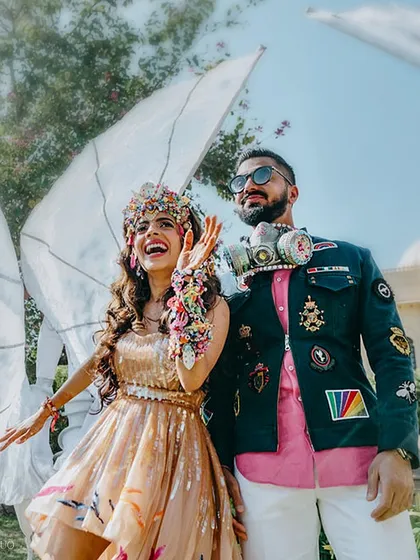 A joyful shot of the couple, with the bride's handmade headpiece and the groom's quirky gas mask accessory on full display. Winged performers add to the surreal, festive atmosphere.