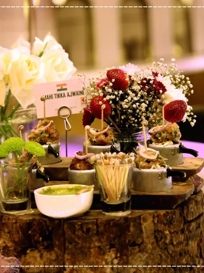 At a recent wedding, we served exquisite appetizers like these Mahi Tikka Ajwaini bites. They were presented on a rustic wooden block with fresh dips and floral arrangements.