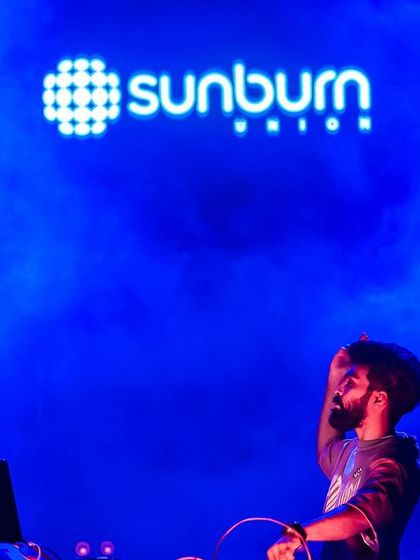 On the mic against the iconic Sunburn logo. The blue smoke and lighting create a powerful and atmospheric image.