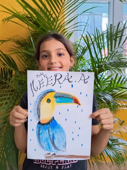 A student displays her vibrant drawing of a toucan, using colored pencils to capture its colorful beak and feathers.