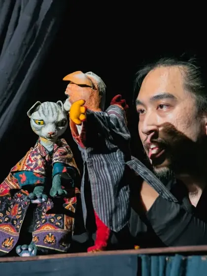 The puppeteer and his two main characters from 'Hiss & Arf'. His direct interaction with the puppets adds another layer to the performance.