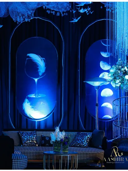 A surreal lounge corner with neon-outlined panels depicting feathers and moons, paired with a modern houndstooth-patterned sofa.