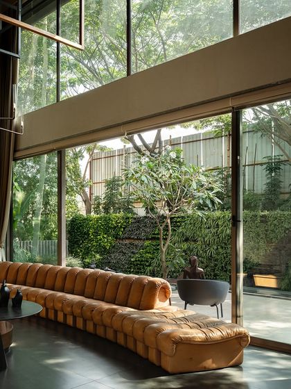 A curved leather sofa in a modern living room facing a wall of glass that reveals a vertical garden and patio. The design ensures that even from deep within the house, the presence of nature is strongly felt.