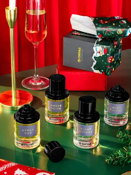 A sophisticated Christmas setup with perfumes, gift boxes, and a glass of champagne. The red and green color palette, along with the warm lighting, creates a classic and elegant holiday atmosphere.