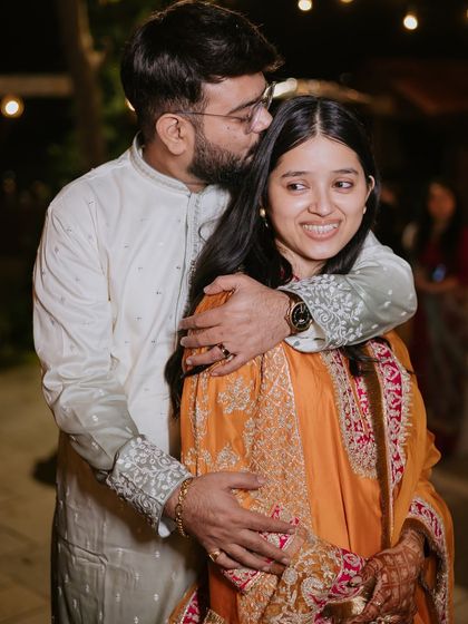 A sweet, candid moment of the groom kissing the bride's head during their intimate Mehendi celebration.