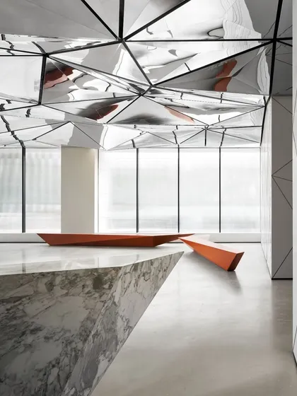 The angular form of the marble reception desk juts into the space, mirroring the sharp lines of the ceiling design and reinforcing the project's geometric foundation.
