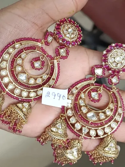 A unique pair of spiral-shaped chandbali earrings with ruby-colored beads and kundan work, finished with small jhumkis.