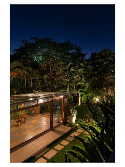 As dusk settles, the Komorebi Pavilion glows from within, highlighting the warm wooden structural elements. The surrounding garden is subtly lit, creating a serene and magical atmosphere that extends the usability of the space into the evening.