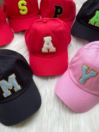 A top-down view of several custom initial caps, displaying the variety of bold colors and letters we offer for creating unique, personalized gifts.