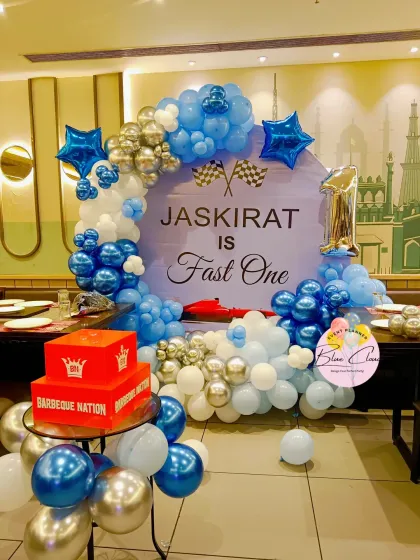 A 'Fast One' race car themed first birthday party. The setup features a custom backdrop with a blue, white, and silver balloon garland.