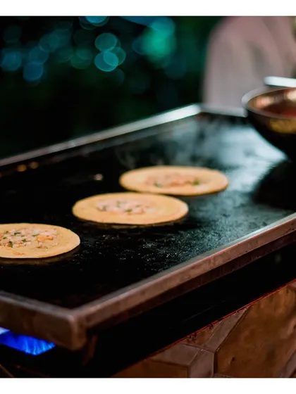 Miniature savoury pancakes are cooked on a hot tawa. This image highlights our ability to create unique and bite sized versions of traditional dishes at our live stations, perfect for passing around.