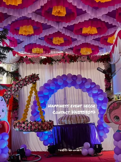 A full view of the naming ceremony stage with the hanging cradle. The entire area is decorated with a colorful tent-style ceiling, a balloon arch, and cute baby cutouts, making it a complete package.