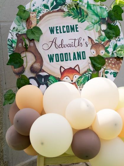 The welcome sign for "Advaith's Woodland," adorned with illustrations of a bear, deer, and fox, and surrounded by a cluster of earth-toned balloons.