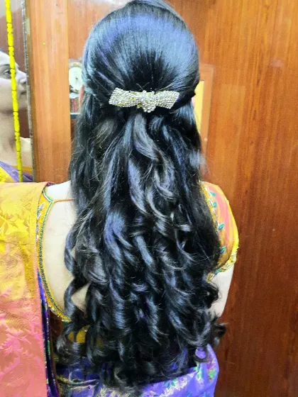 A classic half-up hairstyle with glossy, structured curls. A simple, sparkling bow clip adds a touch of elegance to this timeless look.