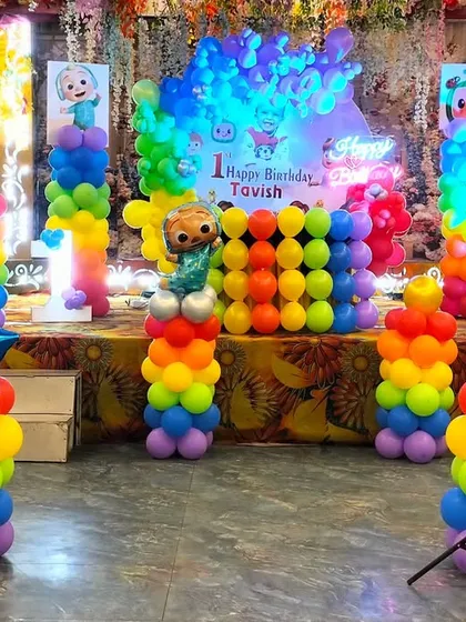 A colorful Cocomelon first birthday stage. The setup is packed with rainbow balloon pillars, character cutouts, and a personalized "Happy Birthday Tavish" backdrop, making it a dream come true for any toddler.