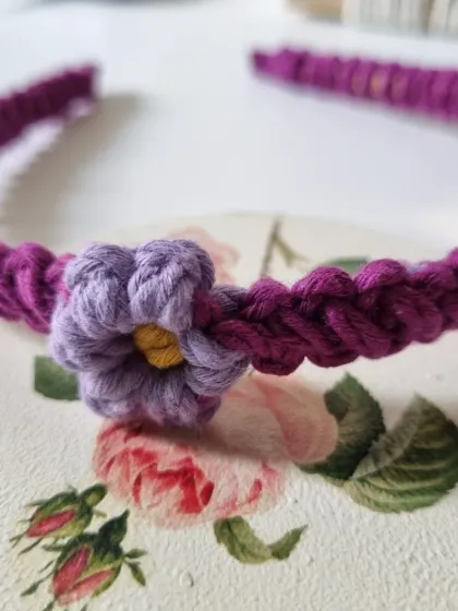 This purple macrame headband features a contrasting lavender flower. The intricate knotting of the band is comfortable to wear all day.