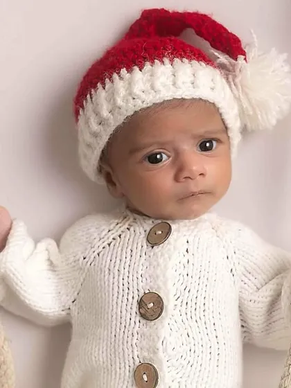 A close-up portrait of the newborn in his Santa hat, looking right at the camera.