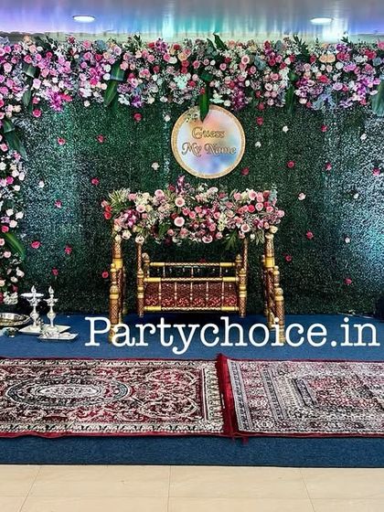 A wide shot of the green floral wall stage for a cradle ceremony, showing how it commands the space and creates a beautiful focal point.