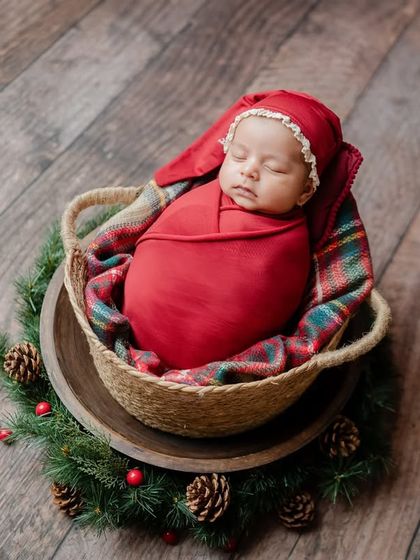 A close-up shot within a basket, this photo highlights the baby's adorable red bonnet and the cozy plaid blanket.