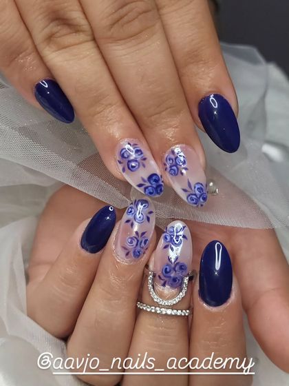 A beautiful set featuring hand-painted blue roses. The combination of solid navy blue nails and accent nails with delicate floral patterns on a clear base is classic and elegant.