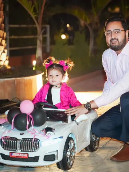 A fun father-daughter portrait. The birthday girl is all smiles in her miniature BMW, posing with her dad during her stylish outdoor birthday event.
