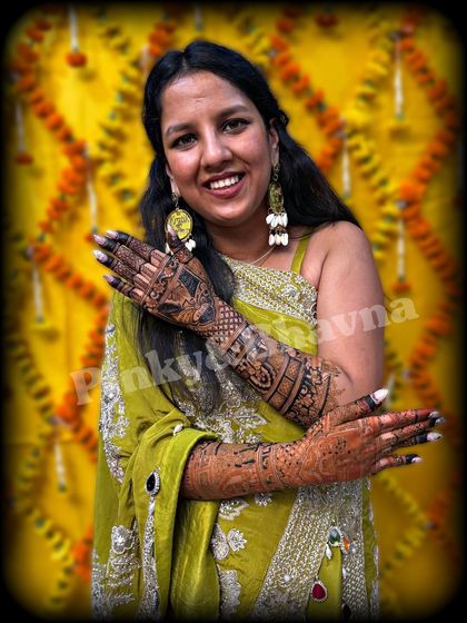 A happy bride posing with her full bridal mehndi. The vibrant yellow background makes her intricate henna art pop.