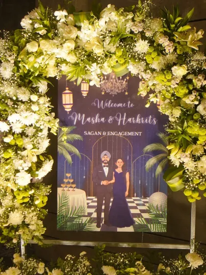 A custom illustrated welcome sign for Masha and Harkrit's Sagan and Engagement, framed by a beautiful arch of fresh white and green florals.
