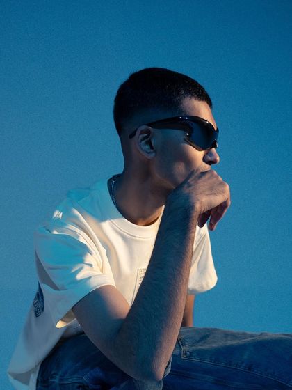A close-up profile shot with a strong blue color grade. The lighting highlights the model's features and the futuristic sunglasses, creating a moody and stylish portrait.