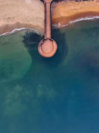 A top-down view of the pier leading to Sinquerim Fort. The clear water and the geometric lines create a visually striking composition.