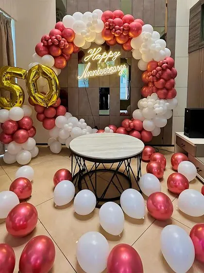 An elegant 50th anniversary decoration for an at-home celebration. This setup is built around a circular frame with a chrome red and white balloon arch, a central 'Happy Anniversary' neon sign, and large '50' foil balloons.