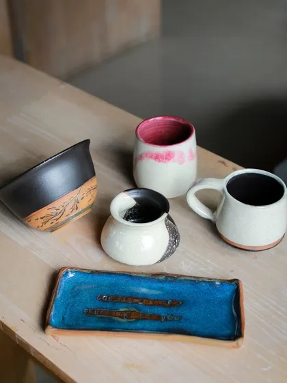 A stylish set of student work, featuring a rectangular tray with a brilliant blue glaze, a carved bowl, and mugs with contrasting colors.